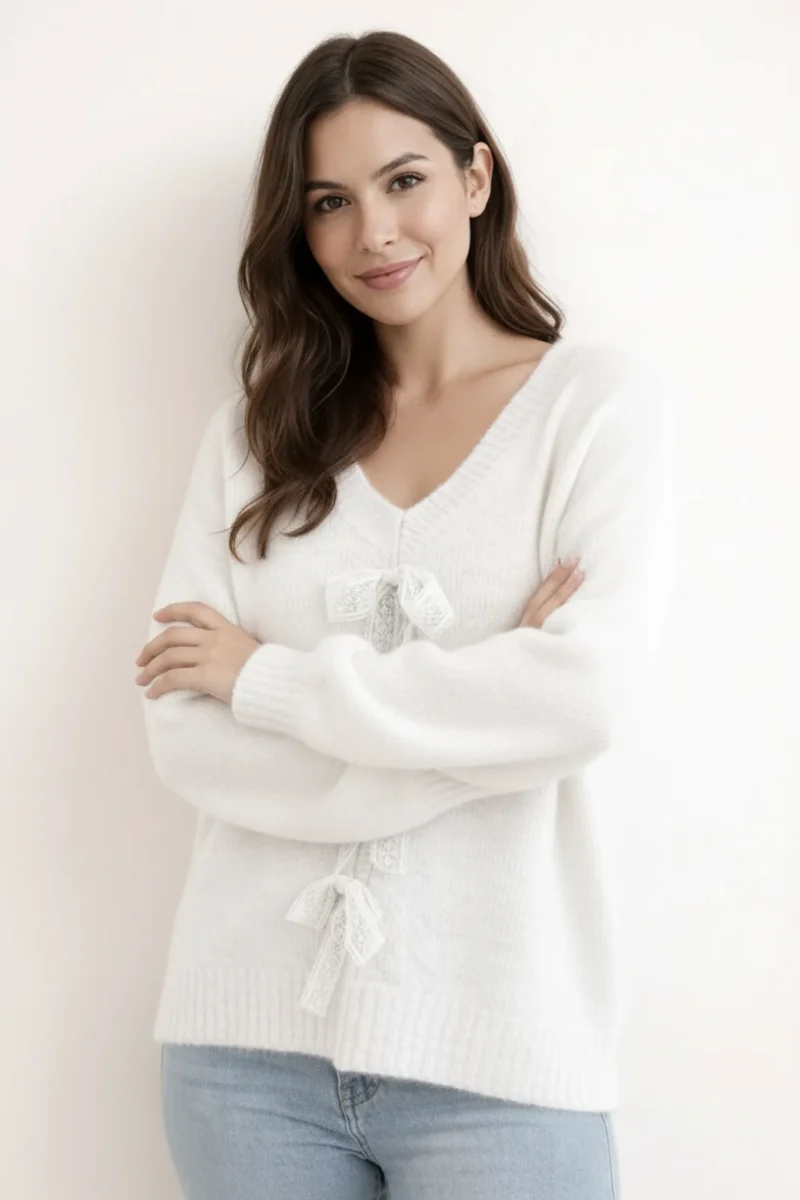 Elegancki sweter damski z koronkowymi detalami, gładki materiał w białym kolorze, blisko ujęcie na ozdobne kokardy.