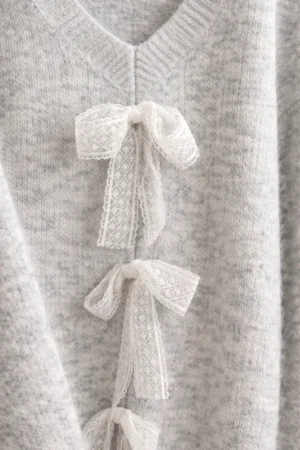 Szary damski sweter z koronkowymi kokardami, dekolt w serek, detal materiału i prosty krój.