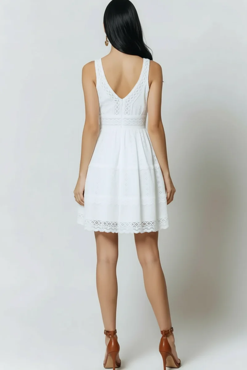 Kobieta stoi tyłem do widza, prezentując białą, letnią sukienkę mini. Sukienka ma dekolt w ksz