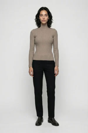 Modelka w beżowym golfie i czarnych spodniach na szarym tle.